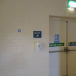 Village hall fire exit, perimeter wall, showing one-way markings and hand-sanitiser station