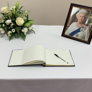 Photo of the parish book of condolence on a table with a flower arrangement and a picture of Queen Elizabeth II